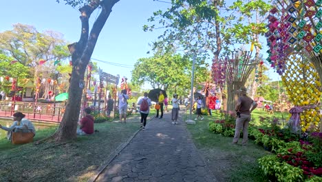 visitors enjoy a sunny day at rama ix park, bangkok, surrounded by vibrant flowers and lush greenery. the atmosphere is lively and serene