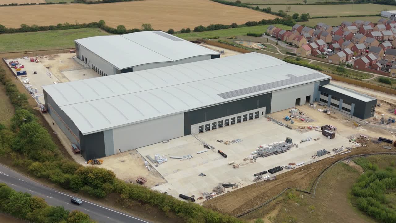 Aerial drone view of large industrial factories and heavy goods vehicles with trailers transporting products near main highway in rural England UK