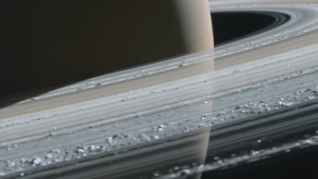 Telecamera che scorre lungo il piano dell'anello nello spazio, rivelando il bordo di un gigante gassoso e mostrando le texture e gli ammassi degli anelli.