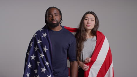 retrato de estudio de una pareja multicultural envuelta en la bandera estadounidense celebrando el día de la independencia del 4 de julio
