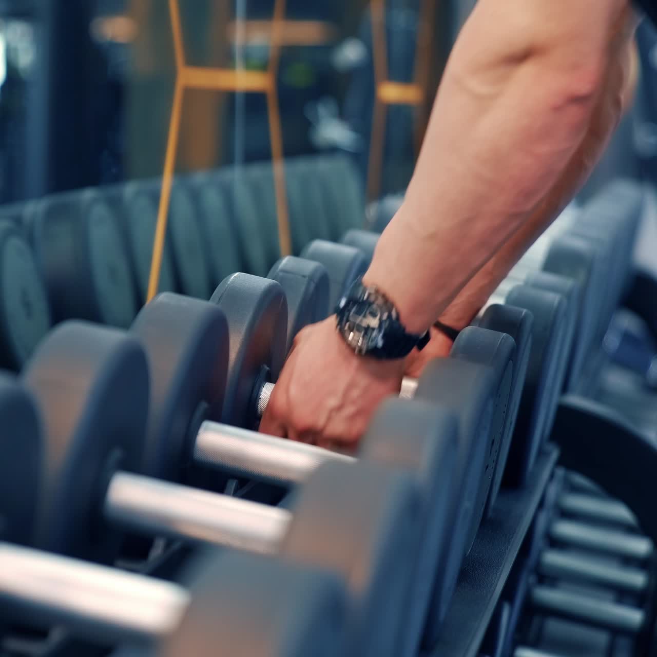 Sportive equipment in gym. Row of heavy dumbbells in fitness center. Muscular bodybuilder taking dumbbells for daily workout. Close-up