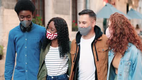 grupo de amigos multiétnicos con máscara y caminando por la calle