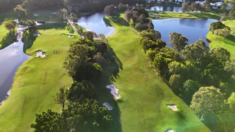 drone captures a sweeping aerial view of a lush golf course with vibrant greenery and water features in gold coast, australia