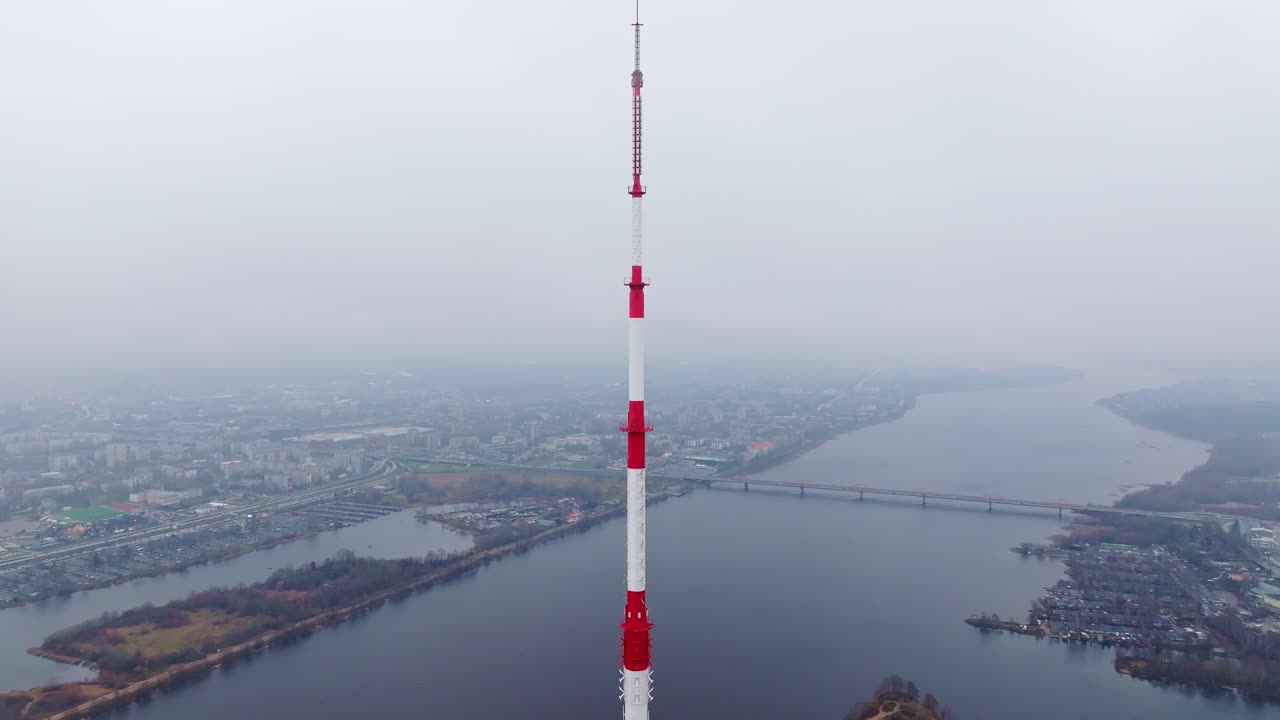 Tall red-white tower fades as drone reveals foggy Riga and quiet Daugava