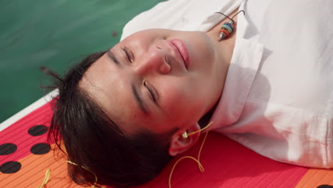 Young-Handsome-Man-Lying-On-Surfboard-In-The-Sea-While-Listening-To-Music