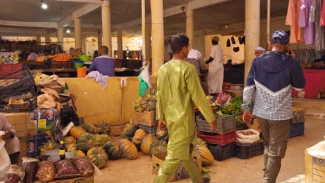 Vegetabele and fruit section at local market on dry and hot day. People in traditional Tuareg clothes passing, selling and buying. Filmed in bazaar in Saharan desert oasis town Timimoun in Algeria