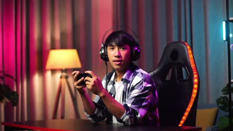 asian teen boy gamer smiling to camera while playing video game on smartphone