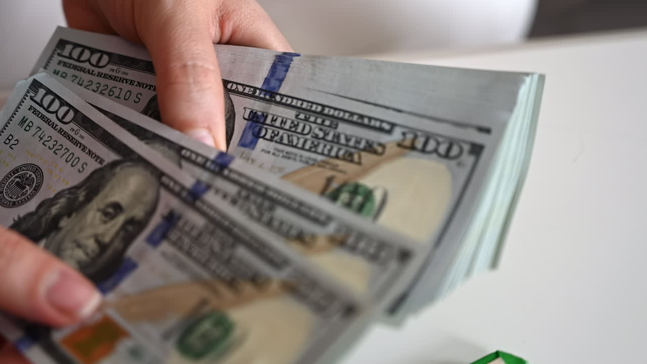 A woman's hands quickly count a stack of one hundred dollar bills against a light background