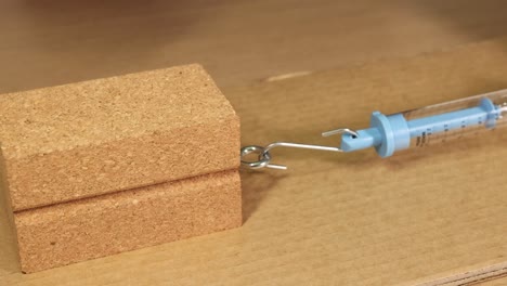 a hand pulls a wooden block using a hook and spring scale on cardboard, demonstrating friction principles