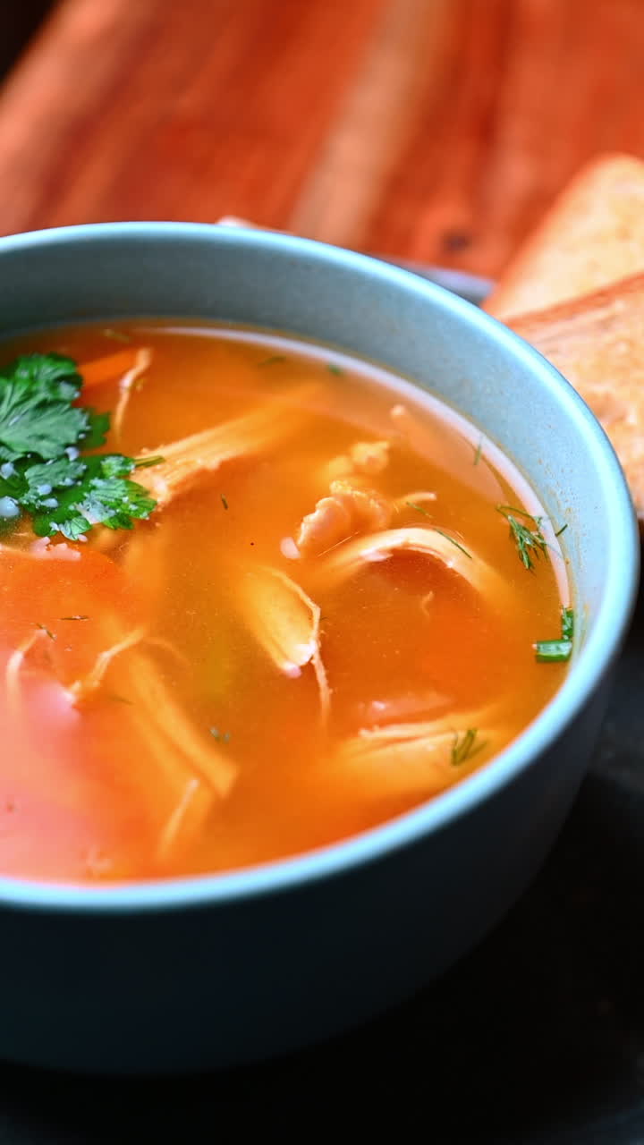 Farverig bouillon med grønt og gulerod. Klar grøntsagsbouillon med urter, gulerodsskiver og varme toner i en keramisk skål
