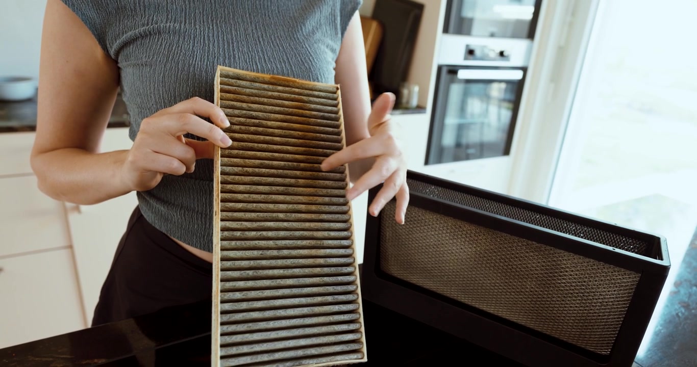 Kvinde holder et meget snavset og fedtet køkkenemhættefilter, der repræsenterer fedtopbygning, forsømt vedligeholdelse, køkkenhygiejne og filterrensning