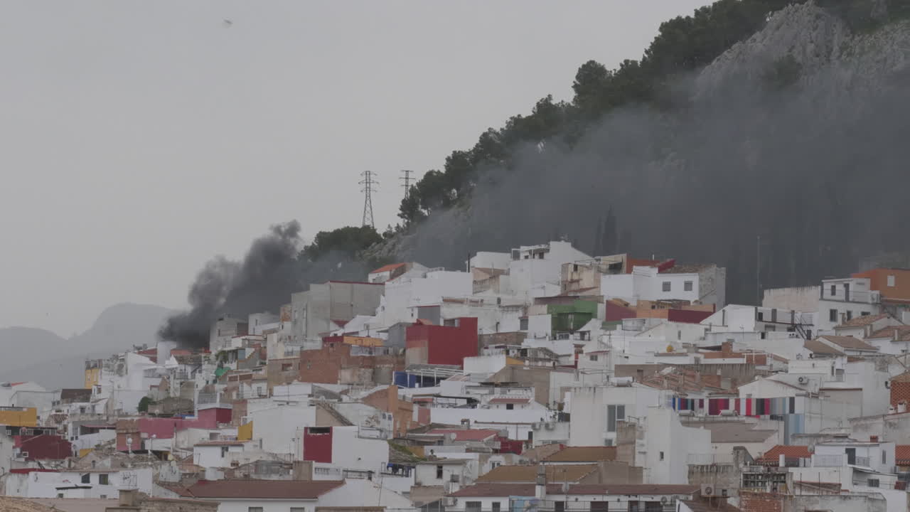 Fumaça preta densa emana de uma casa em chamas em um bairro residencial íngreme de Jaén. Situação de emergência em uma área urbana perto da montanha.