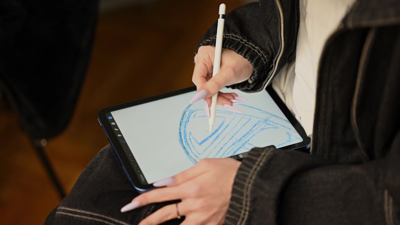 Primer plano de una persona dibujando en una tableta con un lápiz óptico blanco, creando un boceto digital azul con formas geométricas y curvas.