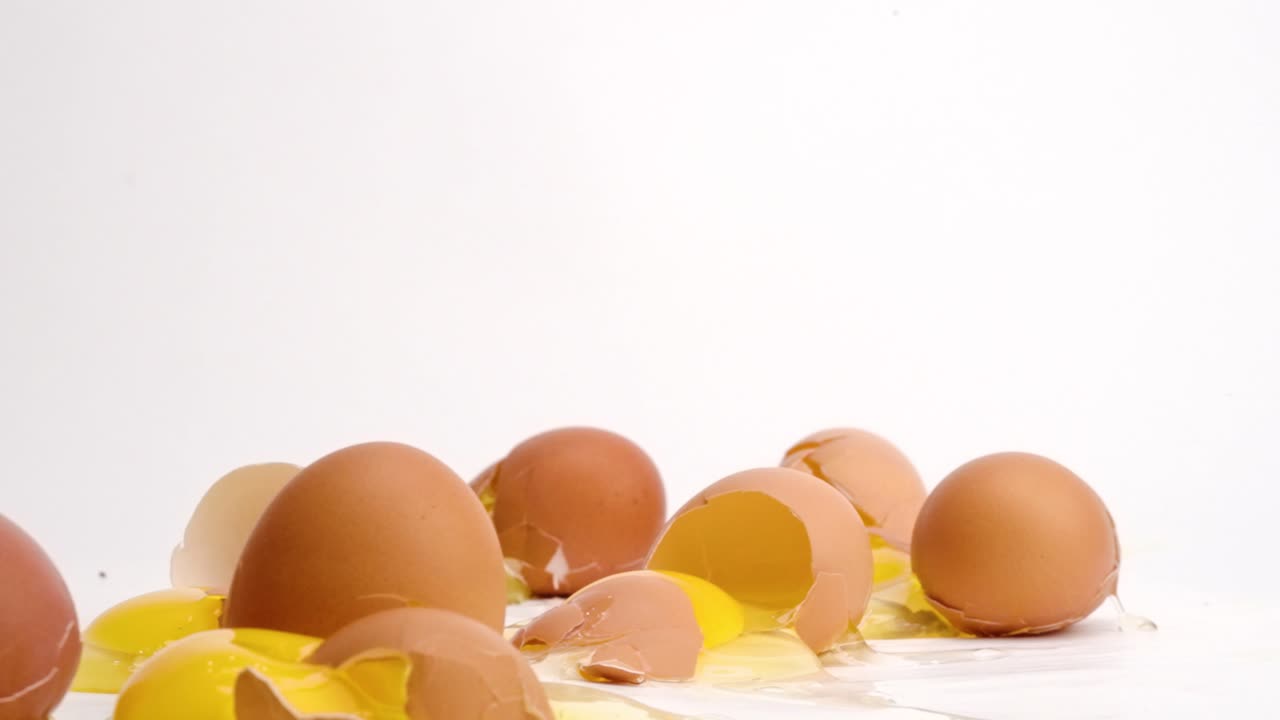 Brown eggs dropped and breaking in slow motion on white studio backdrop in 4k