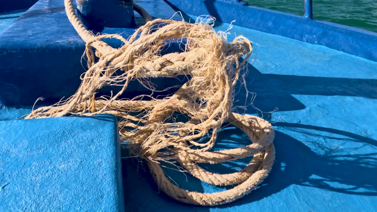 Frayed rope on a blue fishing boat deck in Phuket, Thailand. Bright sunlight highlights textures and colors, creating a nautical atmosphere
