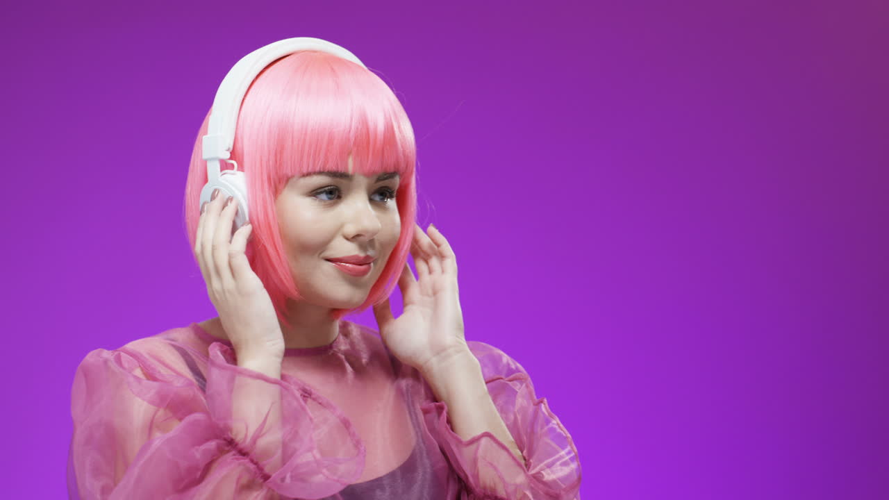 hermosa mujer con una peluca rosa y auriculares, escuchando música y sonriendo a la cámara