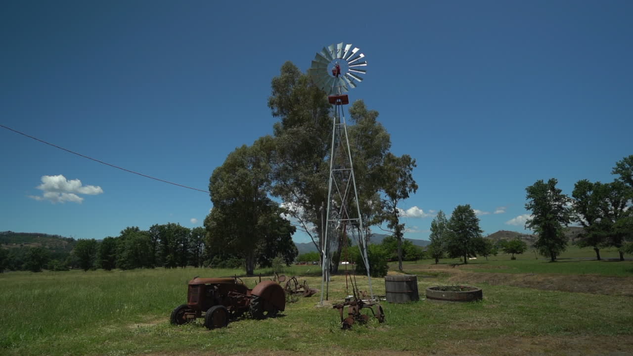 북부 캘리포니아의 전경에 오래된 골동품 트랙터가 있는 시골 목장의 풍차 위로 슬로우 모션 팬