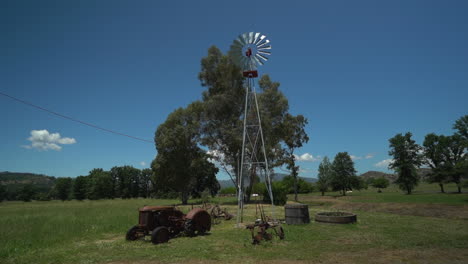 panorámica en cámara lenta de un molino de viento en un rancho rural con un viejo tractor antiguo en primer plano en el norte de california