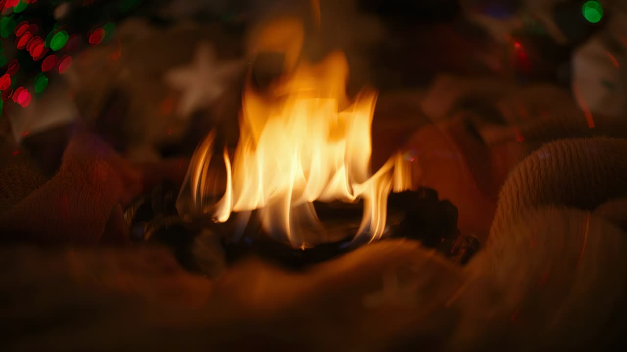 Smoldering charred object releasing small open flame on knit blanket, near star ornament and lights