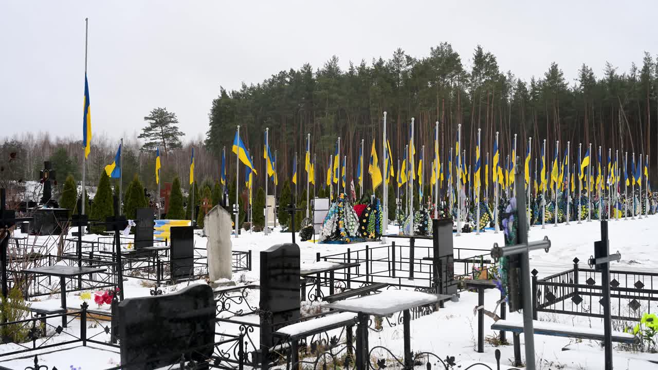 Establishing view of Irpin cemetery on a winter day, with Ukrainian flags standing tall over the graves of soldiers who fell in the Ukraine-Russia war.