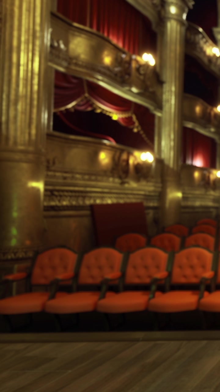 File di sedili arancioni vuoti in un teatro ornato durante un momento di quiete.
