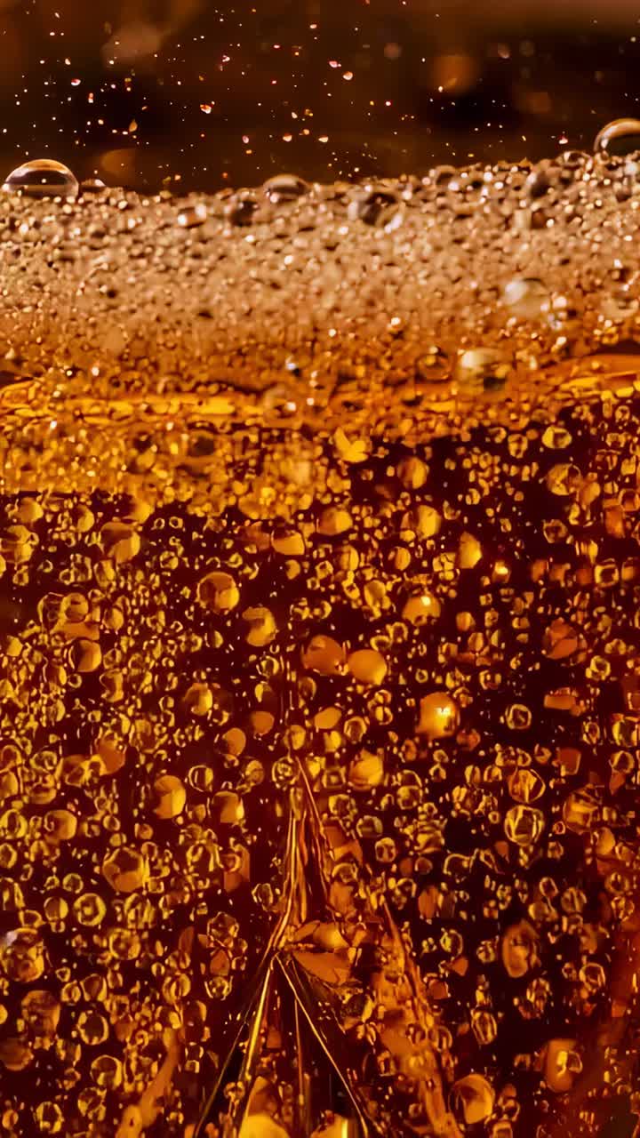 Vertical video: Pouring narrow stream into clear glass causing amber liquid fizzing, forming foam