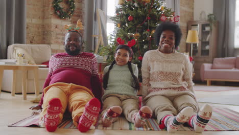 happy african american family sitting by christmas tree and posing for camera