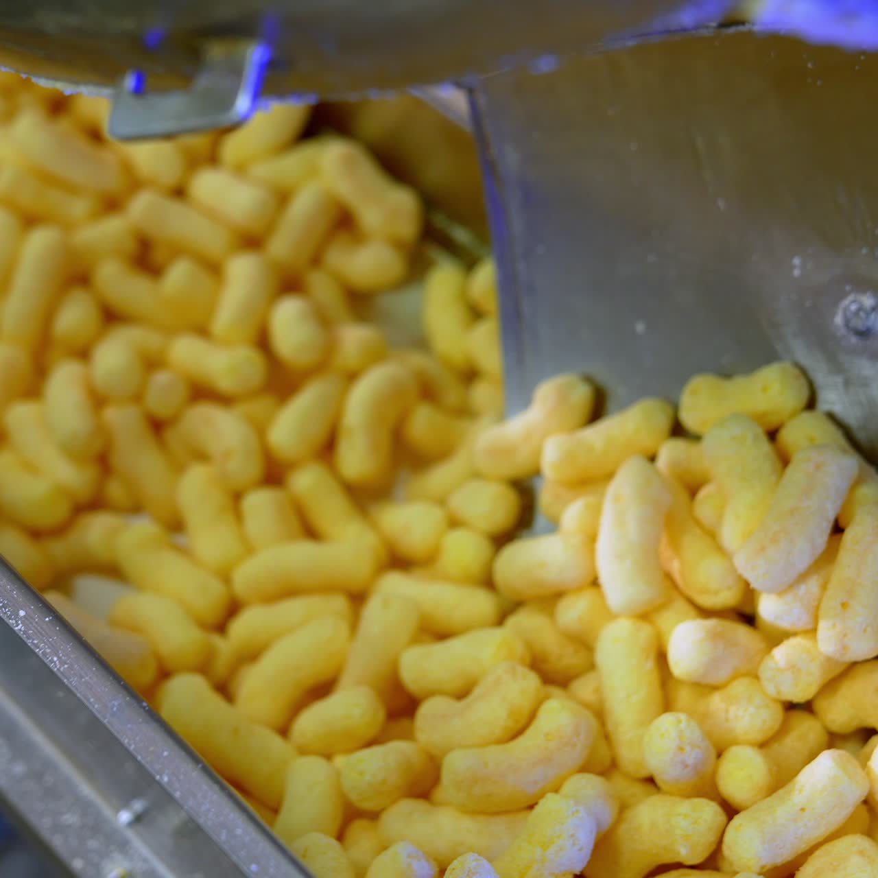 Hand with ladle pushes yellow sweet corn snacks along the conveyor. Close up. Sweet maize sticks production process