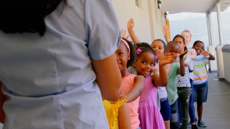 Schoolkids-with-teacher-standing-in-row-with-their-hands-on-shoulder-in-corridor-at-school-4k