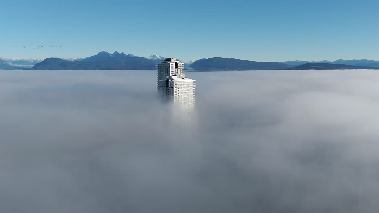 Torre grattacielo sopra una densa coltre di nebbia a Langley, Columbia Britannica, Canada. Montagne lontane sullo sfondo. Ripresa drone orbitante.