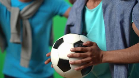 la pelota en manos de un emocionado fanático del fútbol de oriente medio aplaudiendo con un amigo en la pantalla verde. hombres jóvenes irreconocibles apoyando al equipo nacional en el campeonato en el fondo de chromakey.