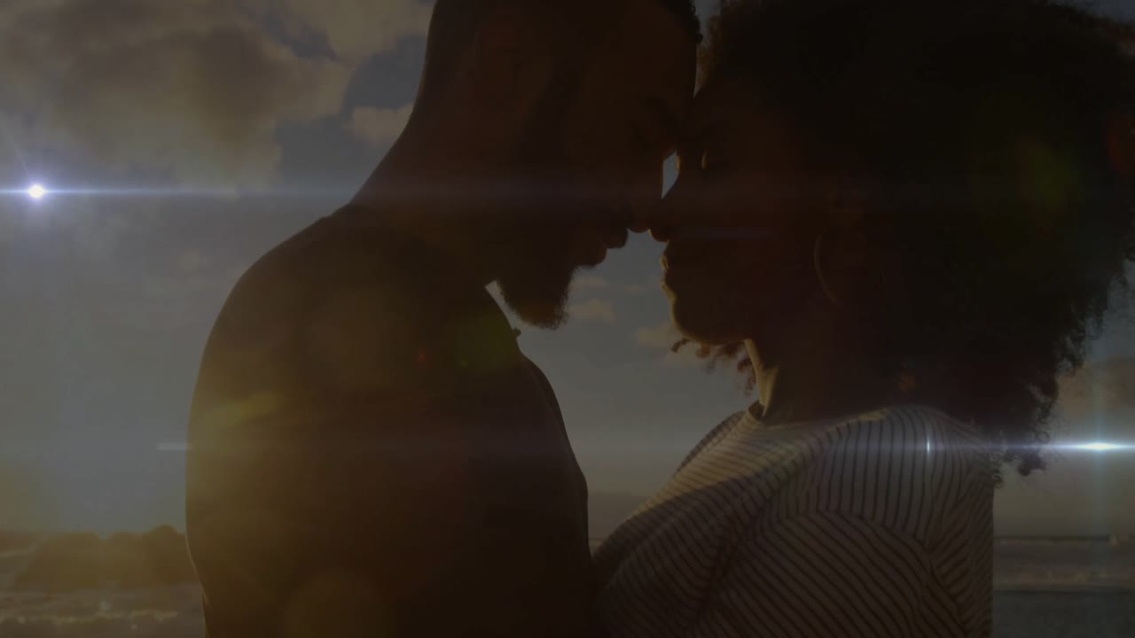 Travel couple touching foreheads as man tilting toward woman at sunset shore, flares dancing