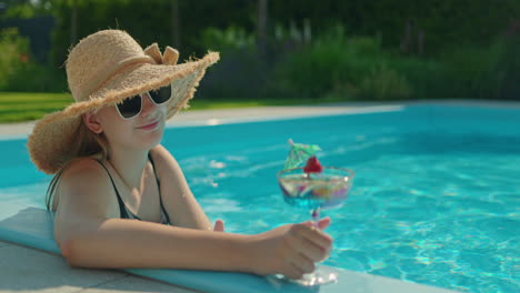 una adolescente relajándose en la piscina con un cóctel.