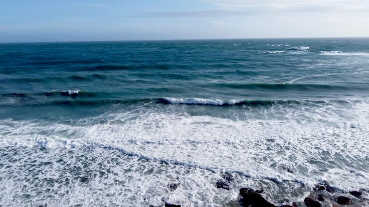 Golven die neerslaan op een zandstrand met rotsen, heldere lucht, luchtfoto