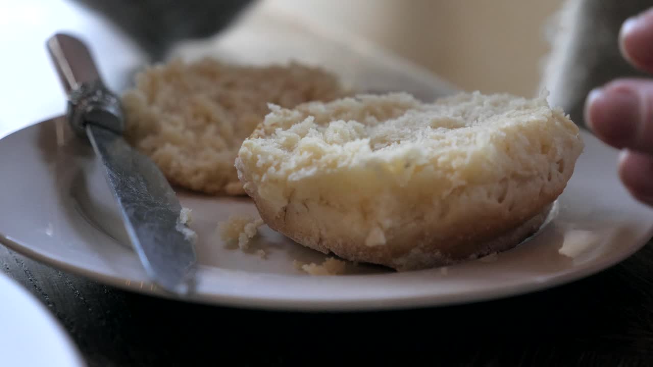 la mano femenina corta el bollo tradicional recién horneado al vapor caliente por la mitad en un plato blanco con un cuchillo para la merienda del té de la tarde