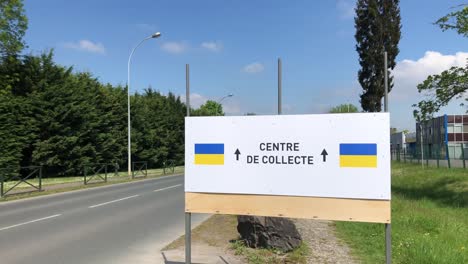 tilt down shot of a banner indicating the direction towards an aid centre for ukrainian refugees at daytime with cars passing by on the road