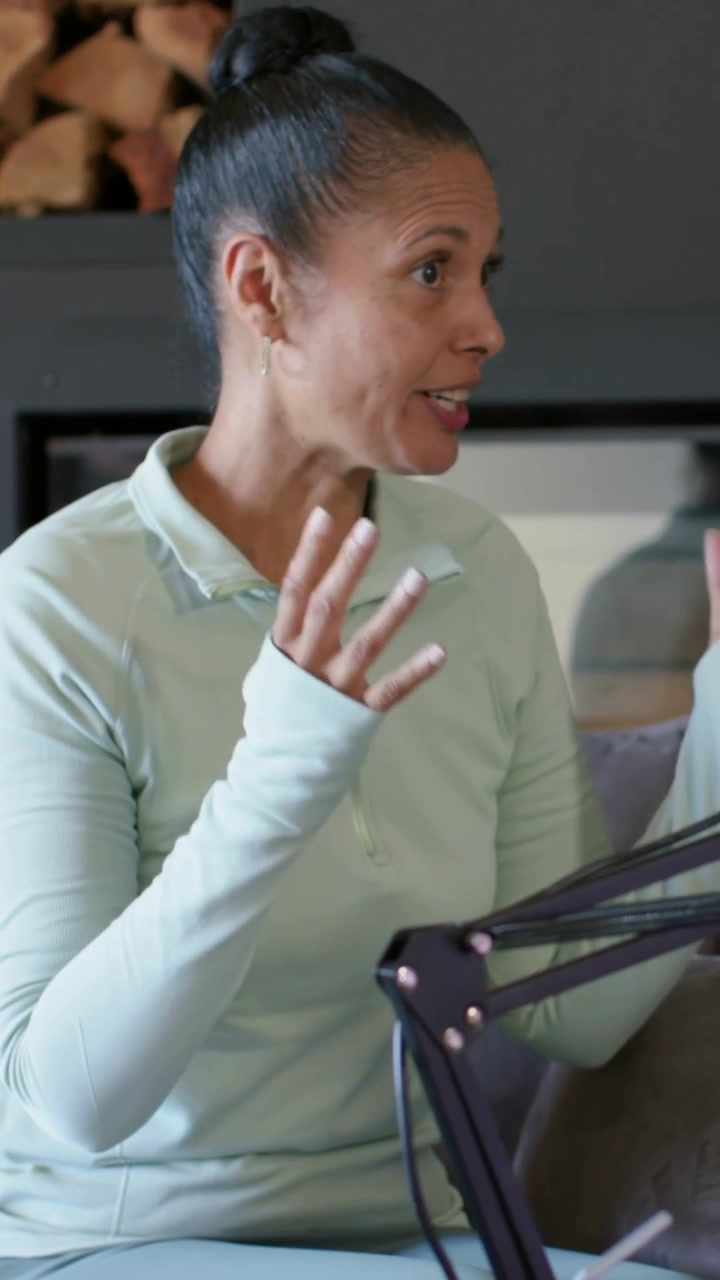Donna che risponde a una domanda del podcast, gesticolando e afferrando una tazza verde mentre la forma d'onda audio reagisce.