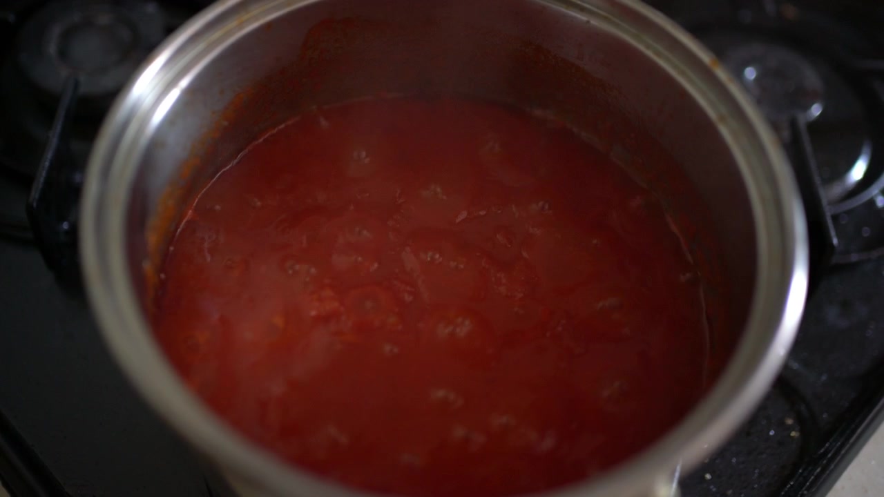 Una pentola di salsa di pomodoro sobbolle su un fornello mentre si addensa lentamente in una pasta, ripresa a mano