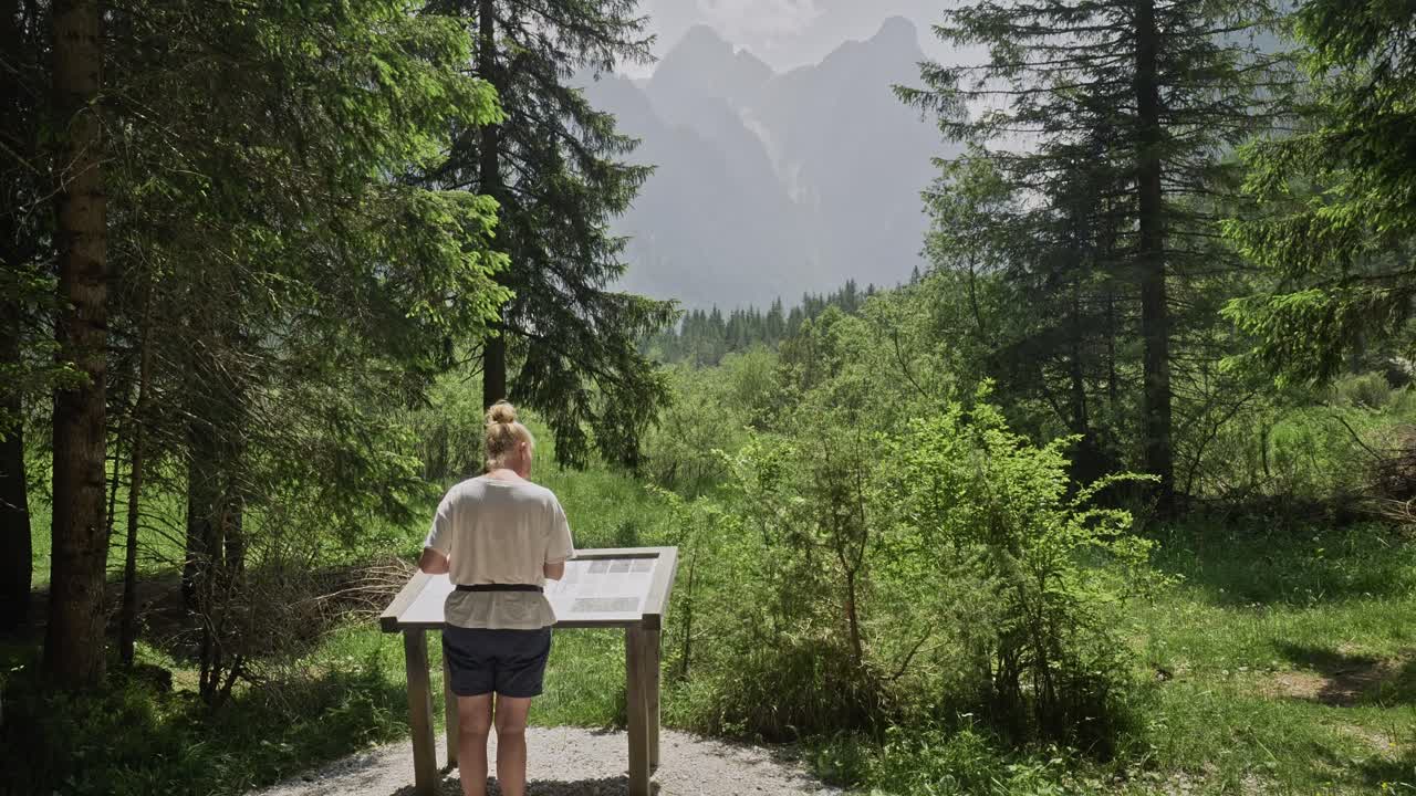 Female nature lover on mountain forest trail reading information board
