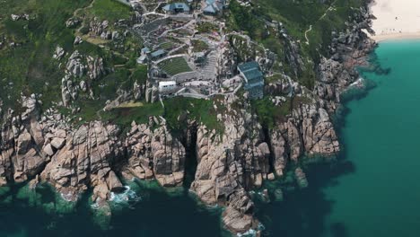 high dolly right above minack theatre revealing turquoise waters and beach