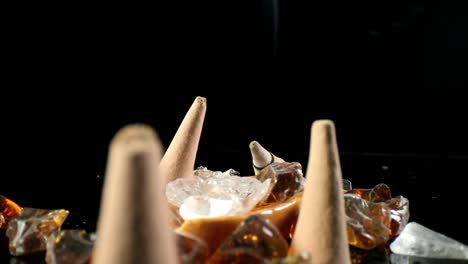 pushing past several unlit incense cones in a decorative rock garden, towards lit cone in back with smoke billowing