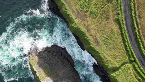 Olas-Rompiendo-Contra-Acantilados-Rocosos-Con-Un-Exuberante-Paisaje-Verde-En-Los-Acantilados-De-Kilkee,-Vista-Aérea