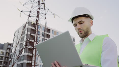 engineer in hard hat and vest using laptop at construction site