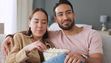 una pareja viendo televisión, comiendo palomitas de maíz.