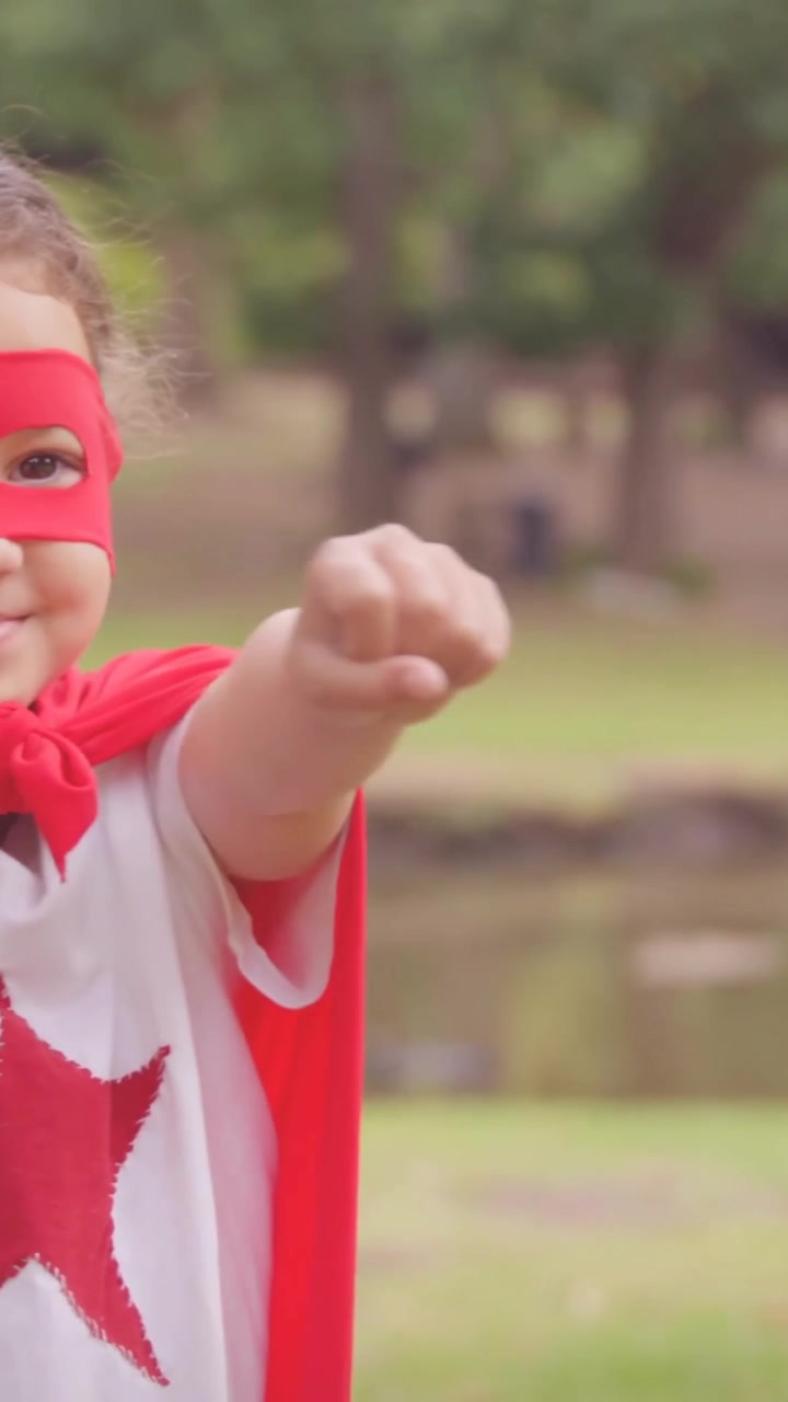 Video vertical: Brazos que hacen flotar suaves corazones rosados mientras un niño con capa roja juega a ser héroe compartiendo amor