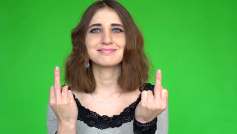young woman showing middle finger gesture while looking at the camera over green background.