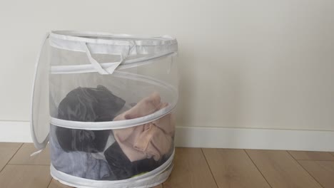 a white laundry basket full of dirty clothes sitting on a wooden floor