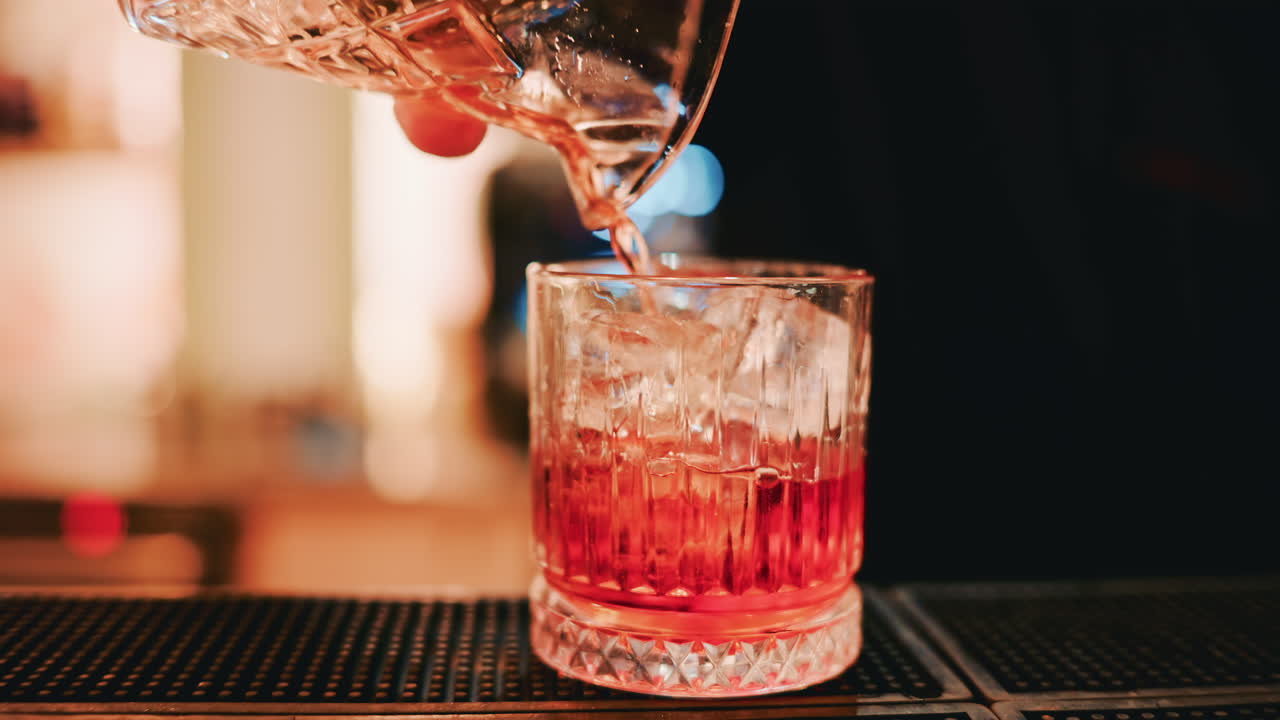 Primo piano di un cocktail appena preparato versato da un mixing glass di cristallo in un tumbler pieno di ghiaccio