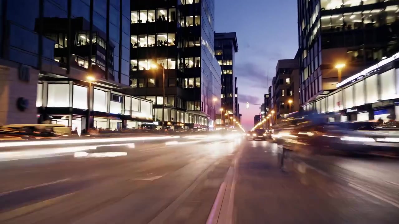 Time-lapse-kuva vilkkaasta kaupungin kadusta moderneine rakennuksineen ja liikkuvine liikenteineen hämärässä