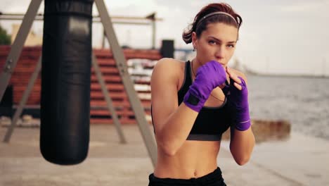 vista de cerca de una mujer joven shadowboxing con sus manos envueltas en cintas de boxeo púrpura mirando a la cámara. hermosa